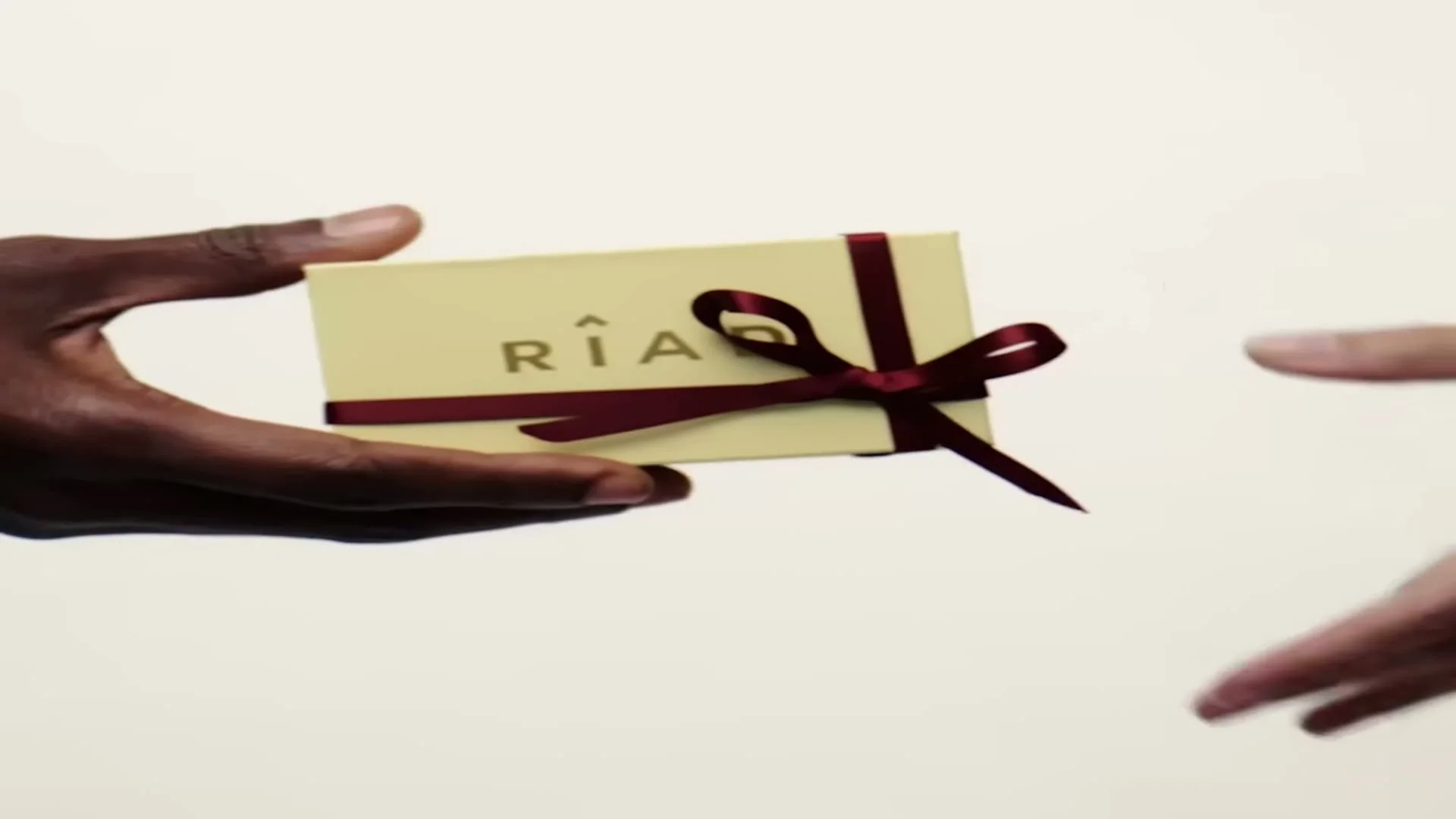 Ett presentkort från Riad med vinröd rosett räcks över mellan två händer